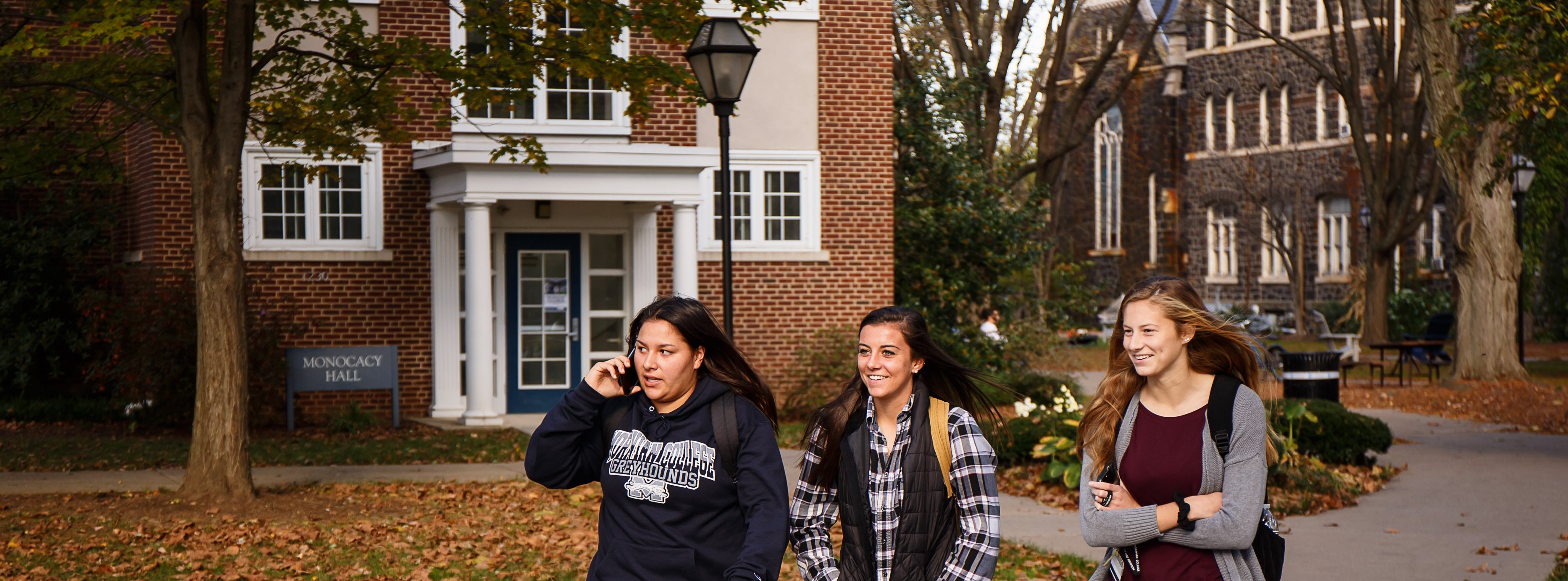 Three students walk in a group out front of Monocacy Hall.