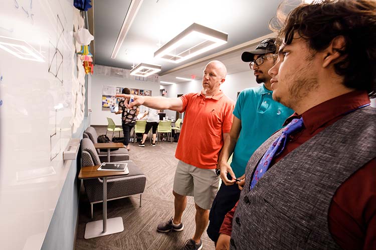 Professor Nate Shank collaborates with two math students at the white board.