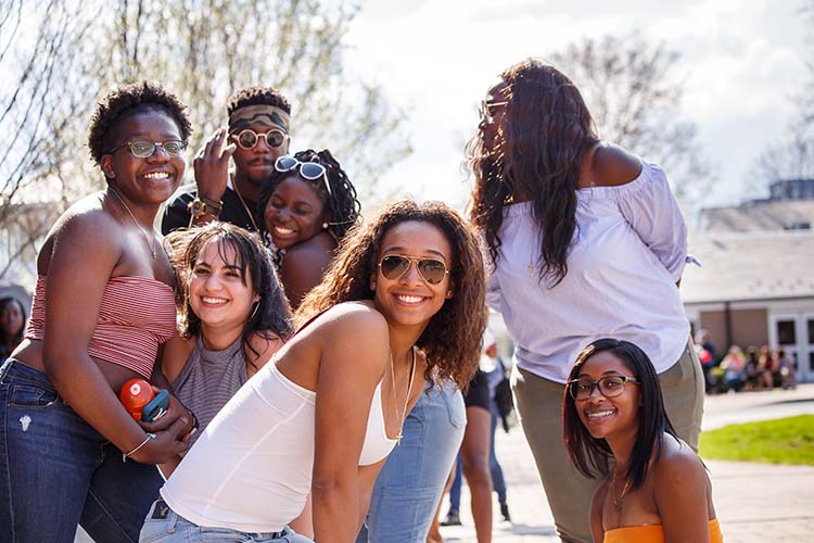 A diverse group of students pose playfully for the camera outside near the HUB.