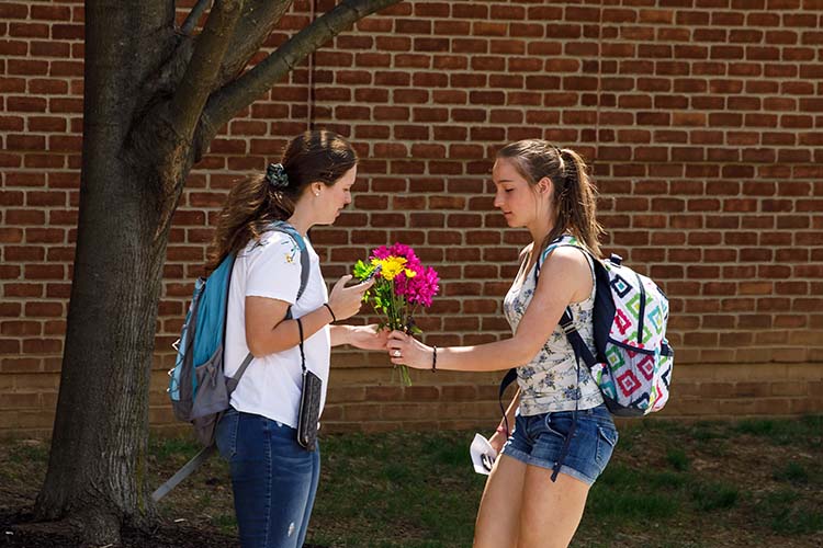 A student gives a bouquet of flowers to her friend.