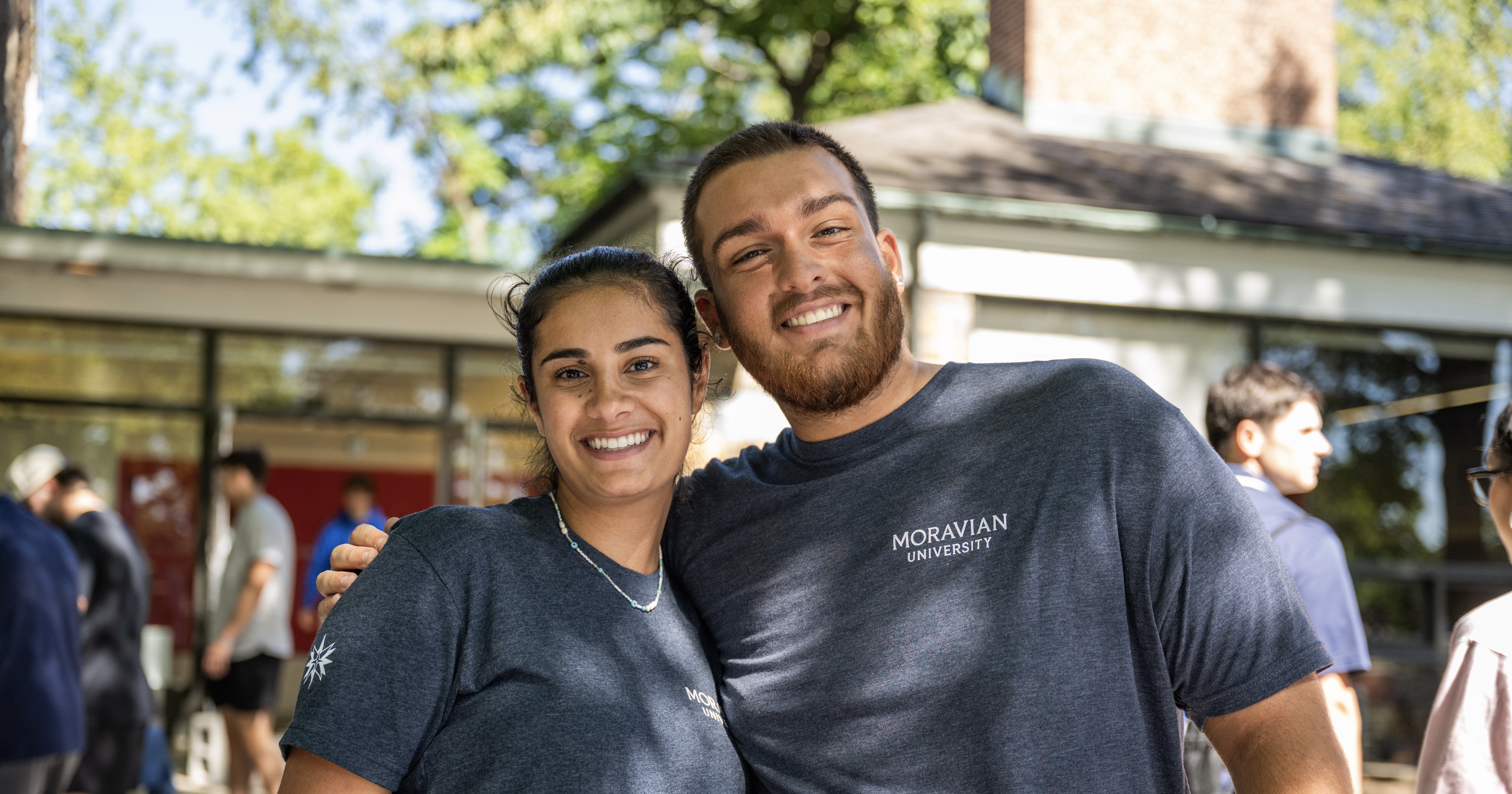 Staff members Ellie and Bubba smiling in a one-armed hug outside the hall on move-in day