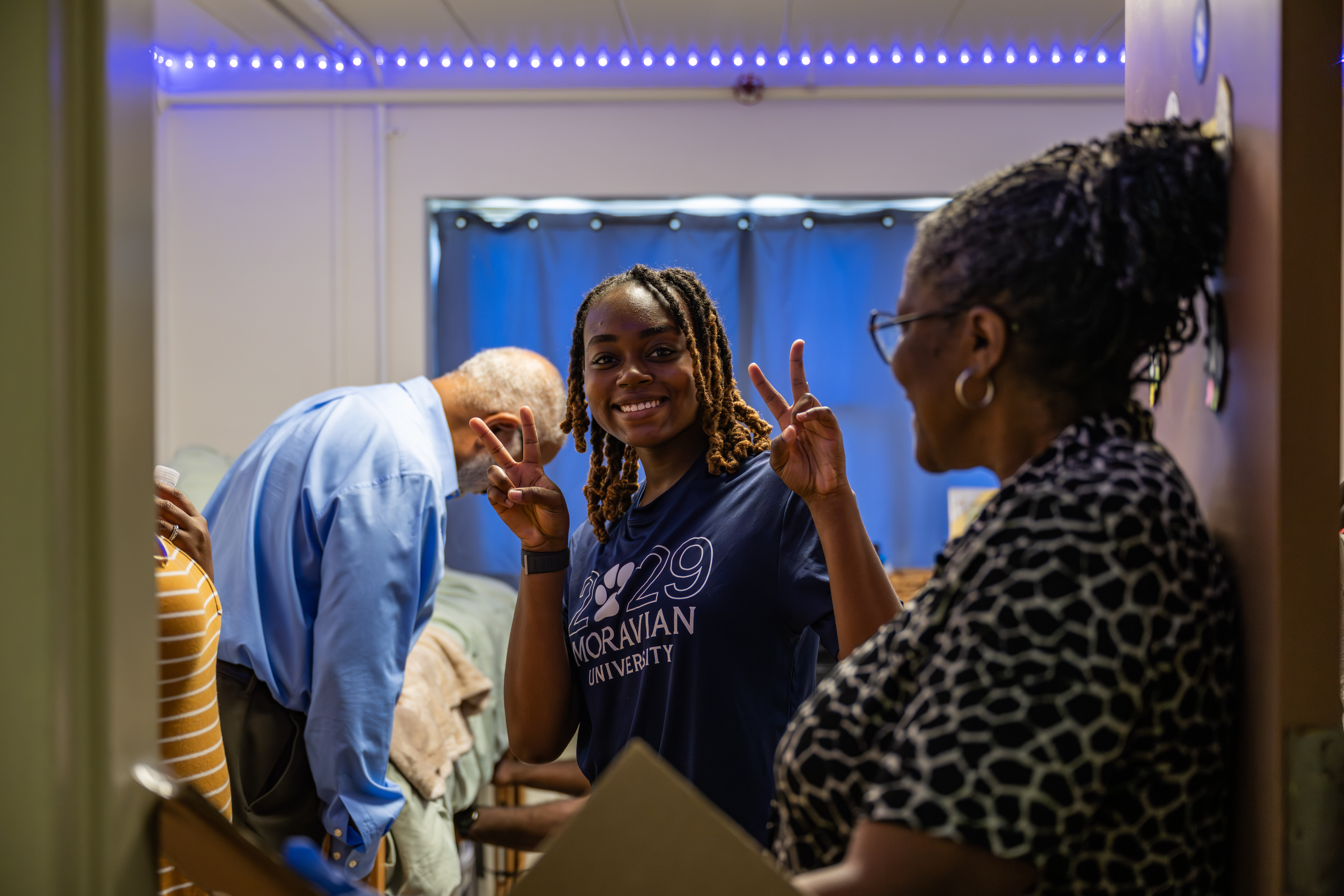resident wearing 2029 Moravian shirt holding up peace signs in her room