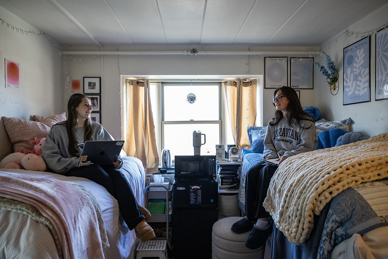 Two roommates on their beds talking to each other across the residence hall bedroom