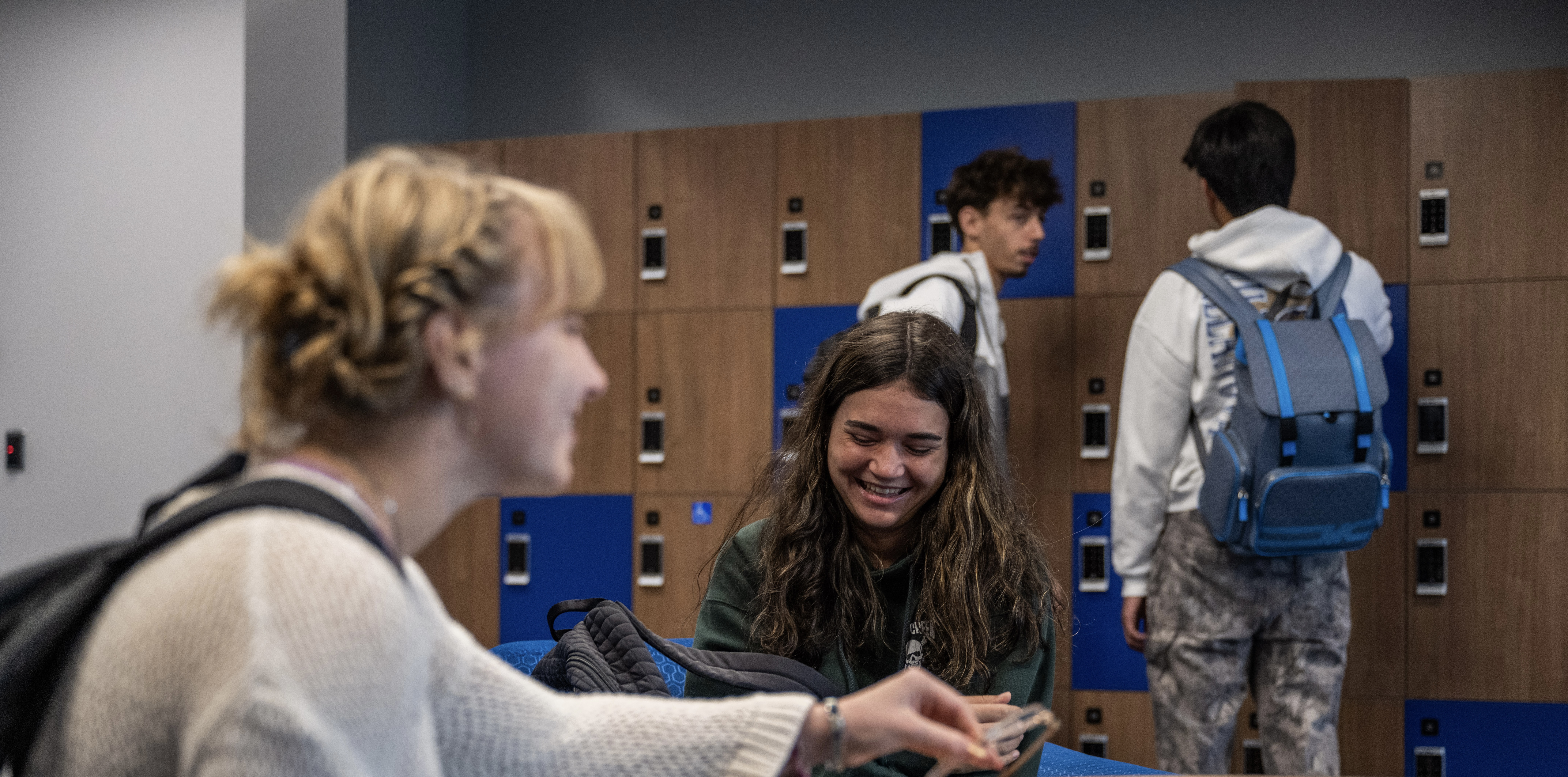 four students nearby the lockers in the commuter lounge on the third floor of the HUB