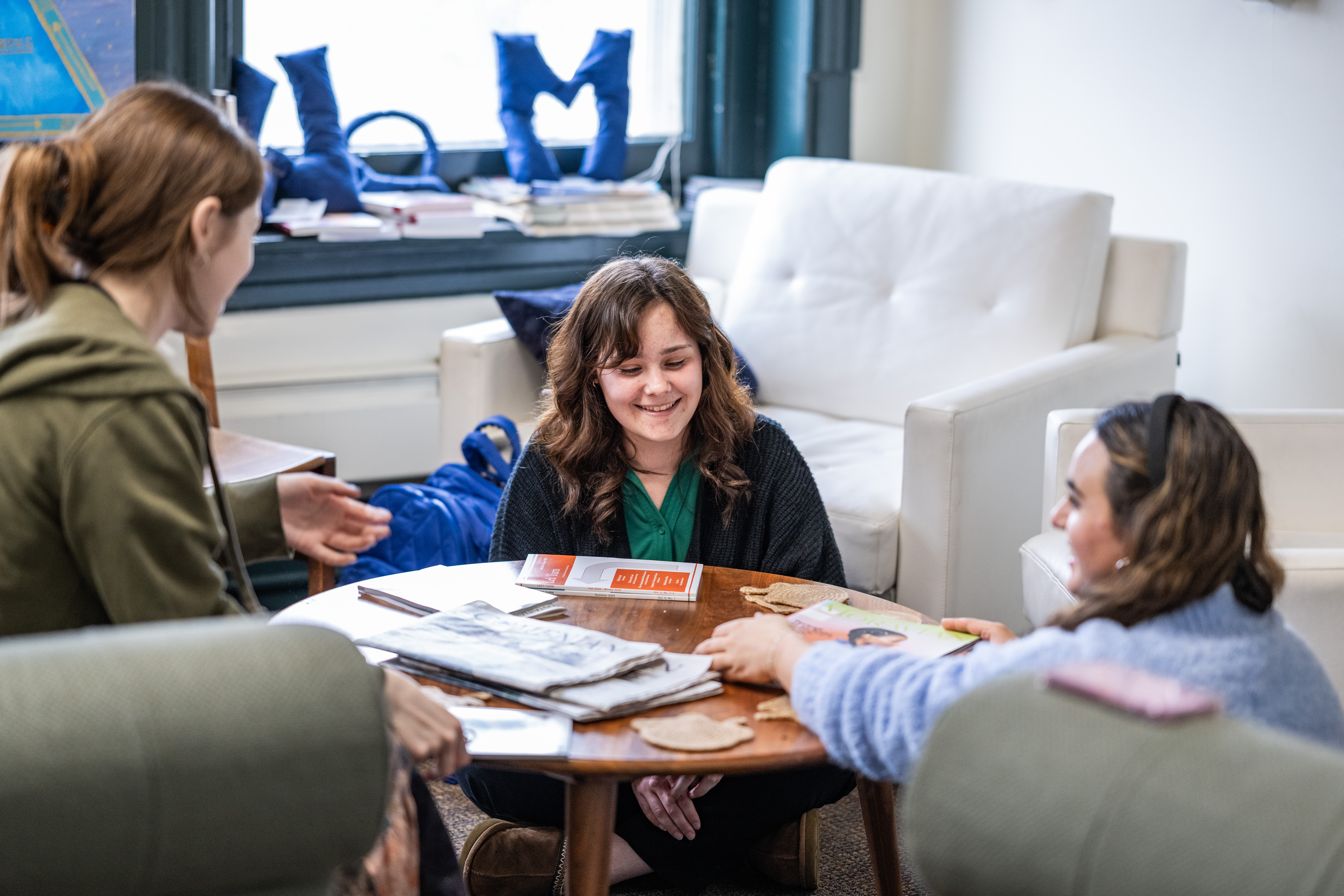 Students sitting on couches in the Moravian University Writing Center. Three women sit around a coffee table, laughing and chatting. Papers are 