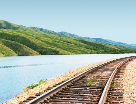 Image of an empty railroad next to a river and green mountains