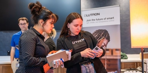 Two women looking at a smartphone together at a Lutron careers event, with a company banner in the background reading "Join the future of smart.